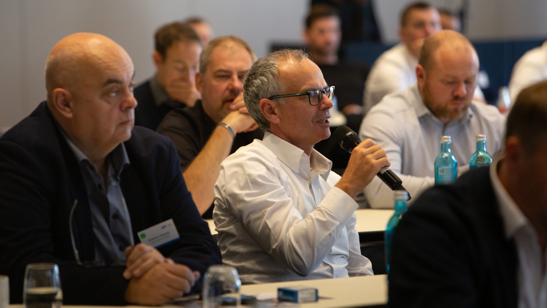 Mann mit Mikrofon sitzend im Plenum