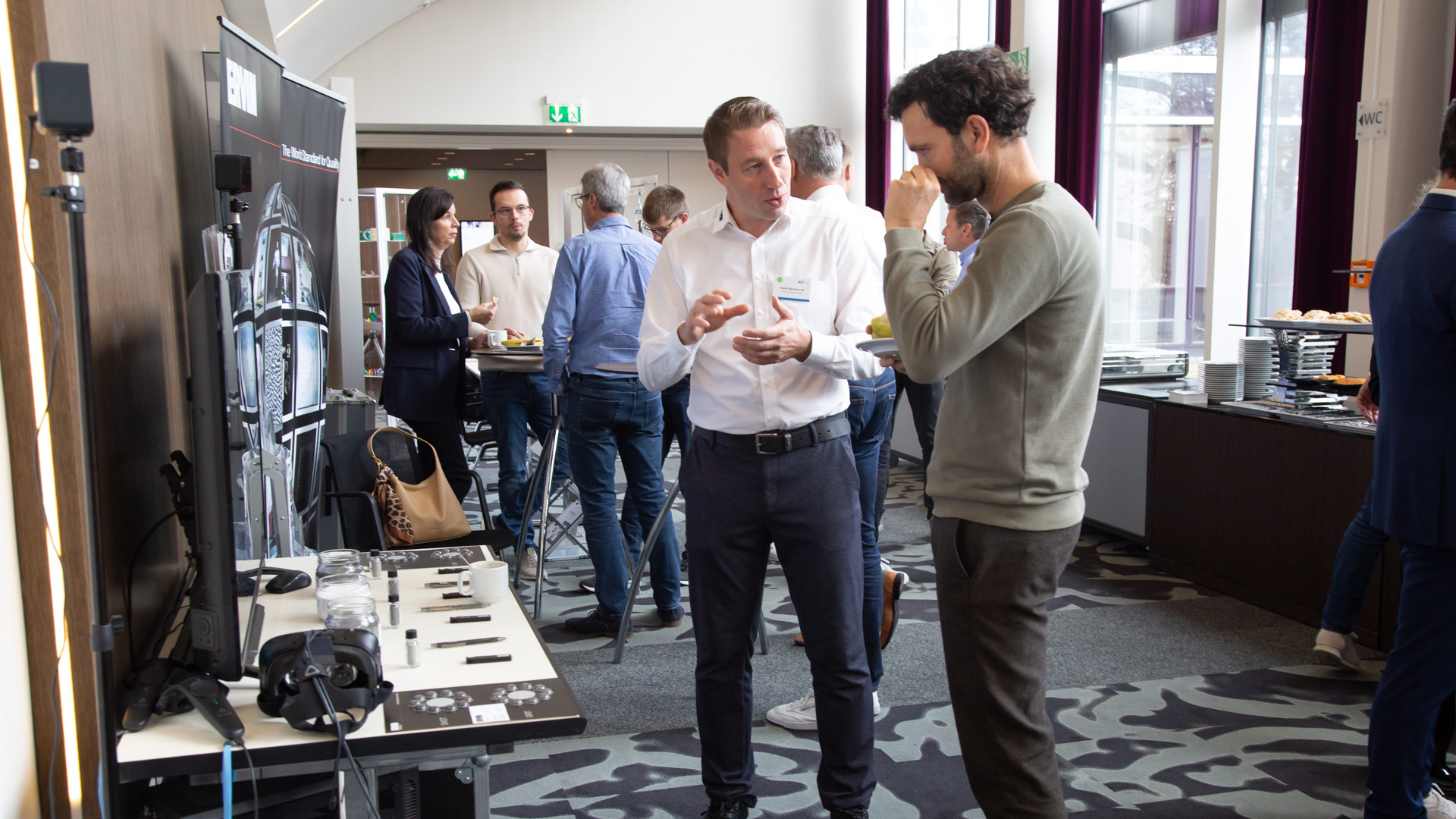 Zwei Herren im Gespräch im Ausstellungsbereich. Im Hintergrund weitere Gesprächsgruppen