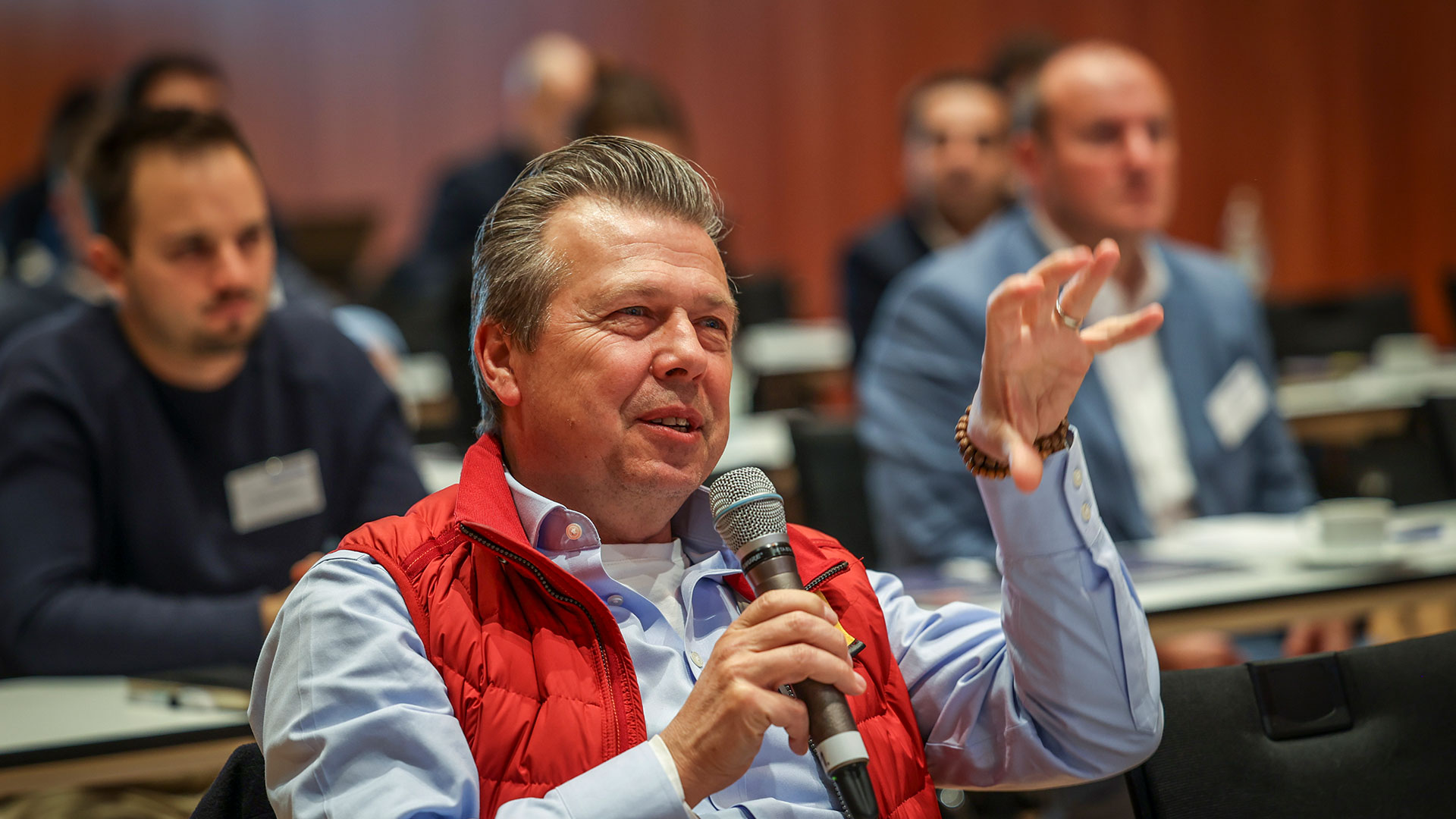 Frage aus dem Publikum. Mann mit Mikrofon sitzend, umrandet von Plenum.  